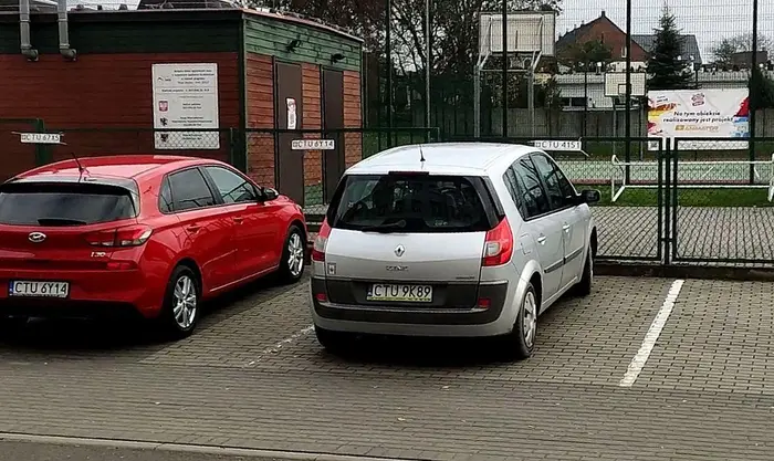 Dziad blokuje miejsce parkingowe - oczywiście nie swoje. Na płocie widac tabliczke z innym nr rej.