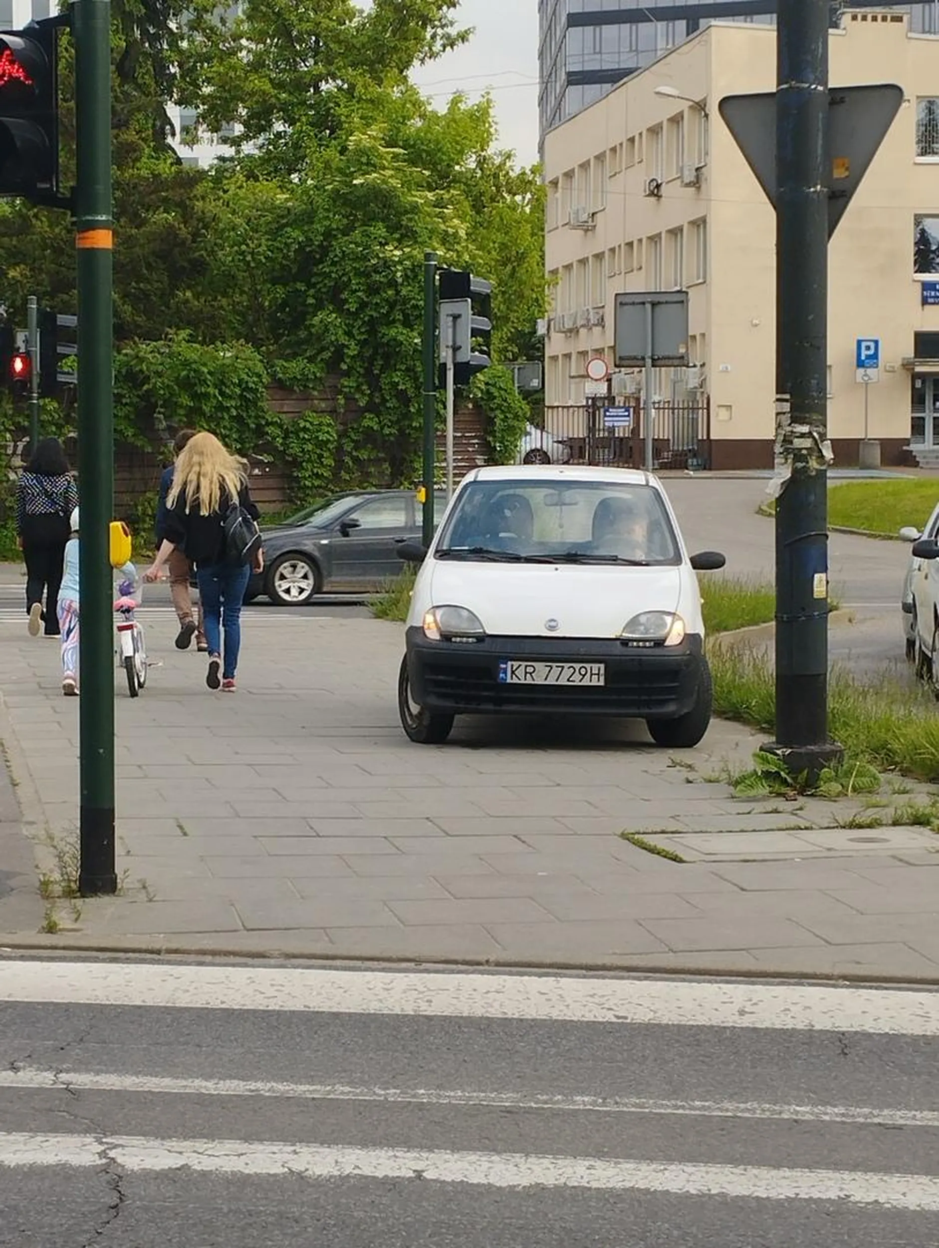 Stoi na chodniku na swoim Fiacie i ogląda instagrama w środku samochodu.