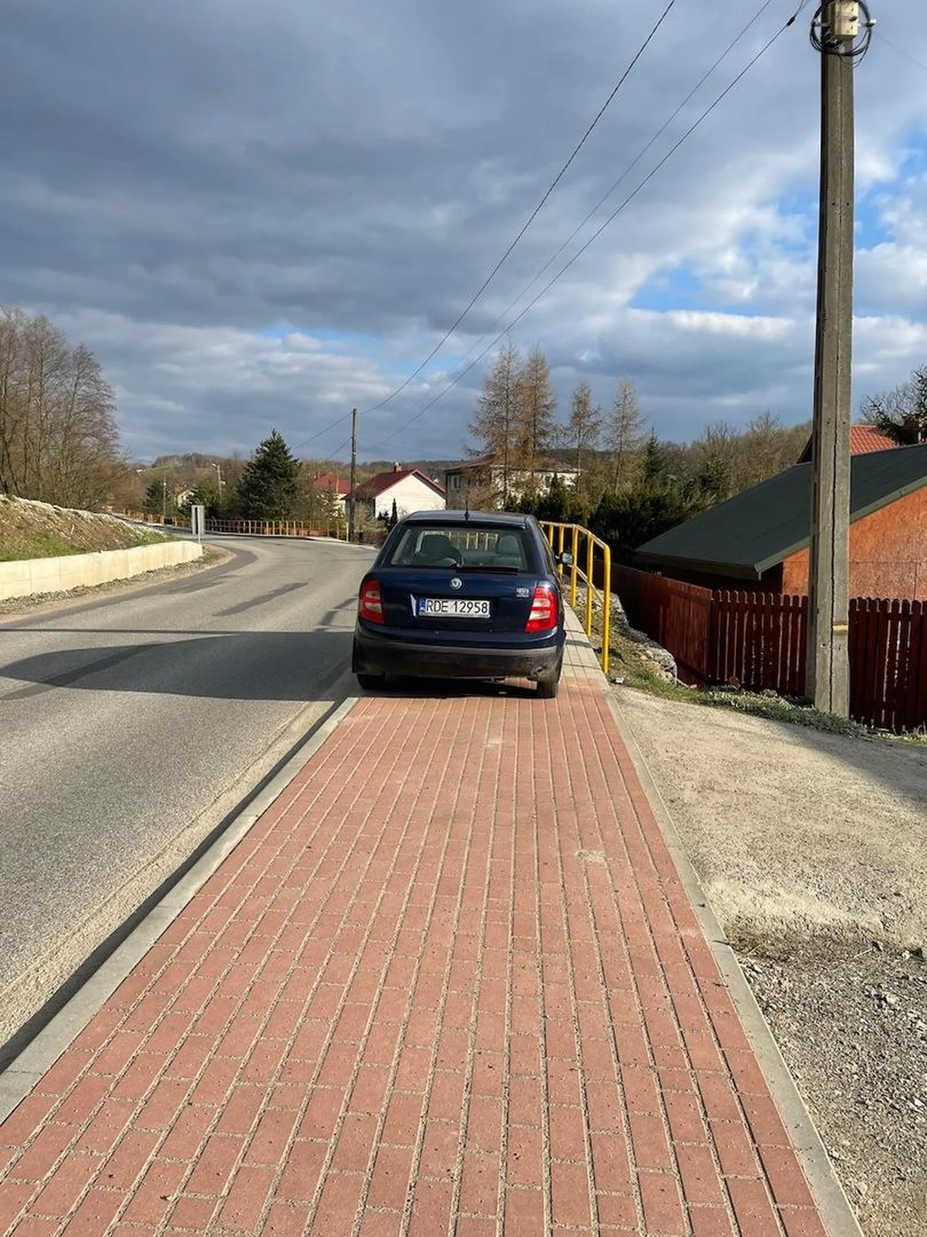 Osoba parkująca Skodą niszczy chodnik oraz zajmuje całą jego szerokość. Auto znajduje się na zakręcie i sprowadza niebezpieczeństwo na ludzi, którzy spacerują chodnikiem. Za II RP tak nie było!