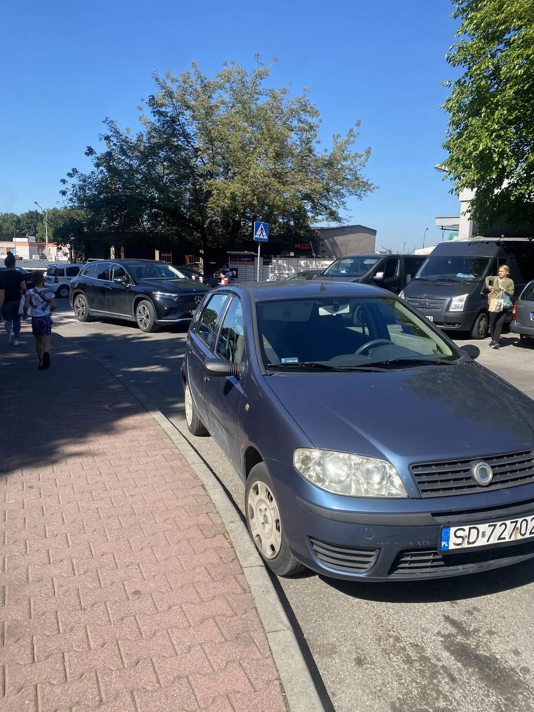 Samochód zaparkowany na jednym pasie ruchu. Oznacza to, że inne samochody muszą wymijać ten pięknie zaparkowany samochód. Do tego auto zasłania przejście dla pieszych, które znajduje się za samochodem jakieś 2 metry. Samochód został zaparkowany w ten sposób, aby Pani nie musiała iść15 kroków z miejsca parkingowego, najchętniej zaparkowałaby pod samym targiem, ale niestety nie można, dlatego Pani wybrała nielegalne miejsce, aby nie musieć robić nawet 5 kroków. Pani która parkowała ten samochód doskonale widziała, że są robione zdjęcia. Następnym razem polecam się odezwać, bo skoro miała pani tyle odwagi, żeby tak bezczelnie zaparkować, to też proszę mieć odwagę podejść :)