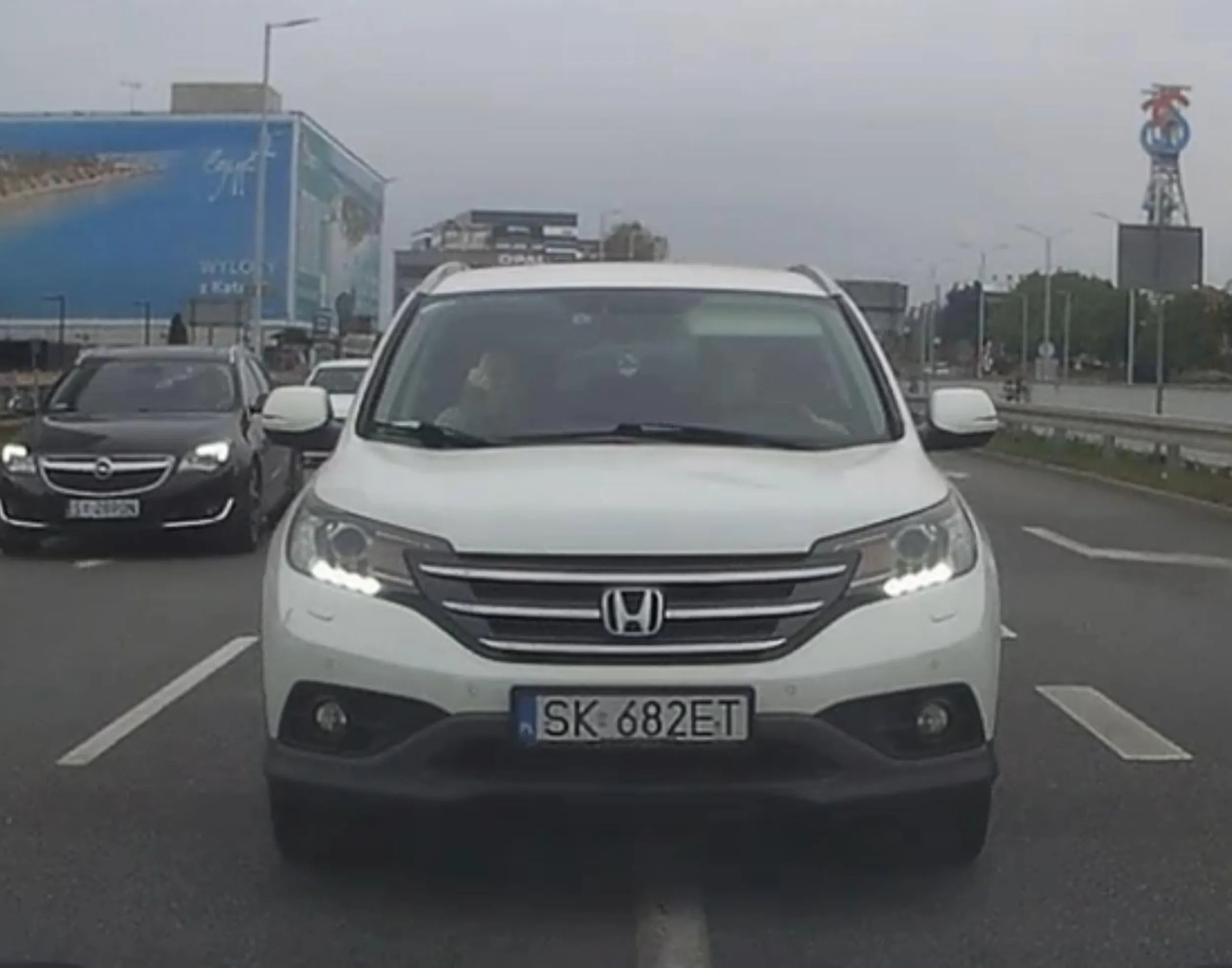 Otyły kierowca i jego pani wyprzedzają na przejściu dla pieszych prawie powodując kolizję z samochodem ciężarowym, który był na drodze z pierwszeństwem przejazdu. Po zwróceniu uwagi klaksonem reagują nerwowo i pani pokazuje środkowy palec.