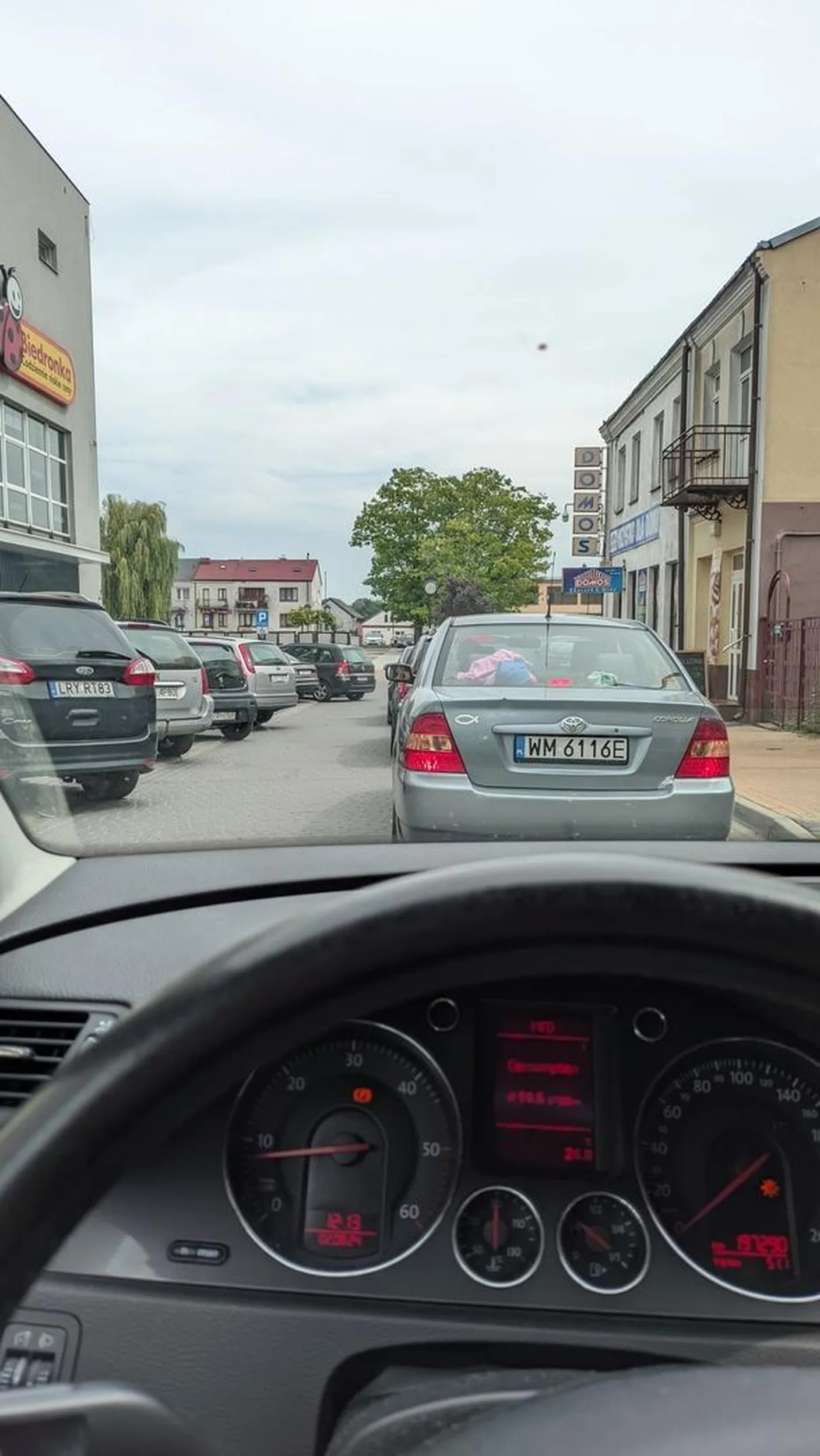 Blokuje cały ruch czekając aż inny kierowca wyjdzie z parkingu by móc zaparkować. Za nim czeka 8 samochodów 5 minut i kierowca nie reaguje na trąbienie.