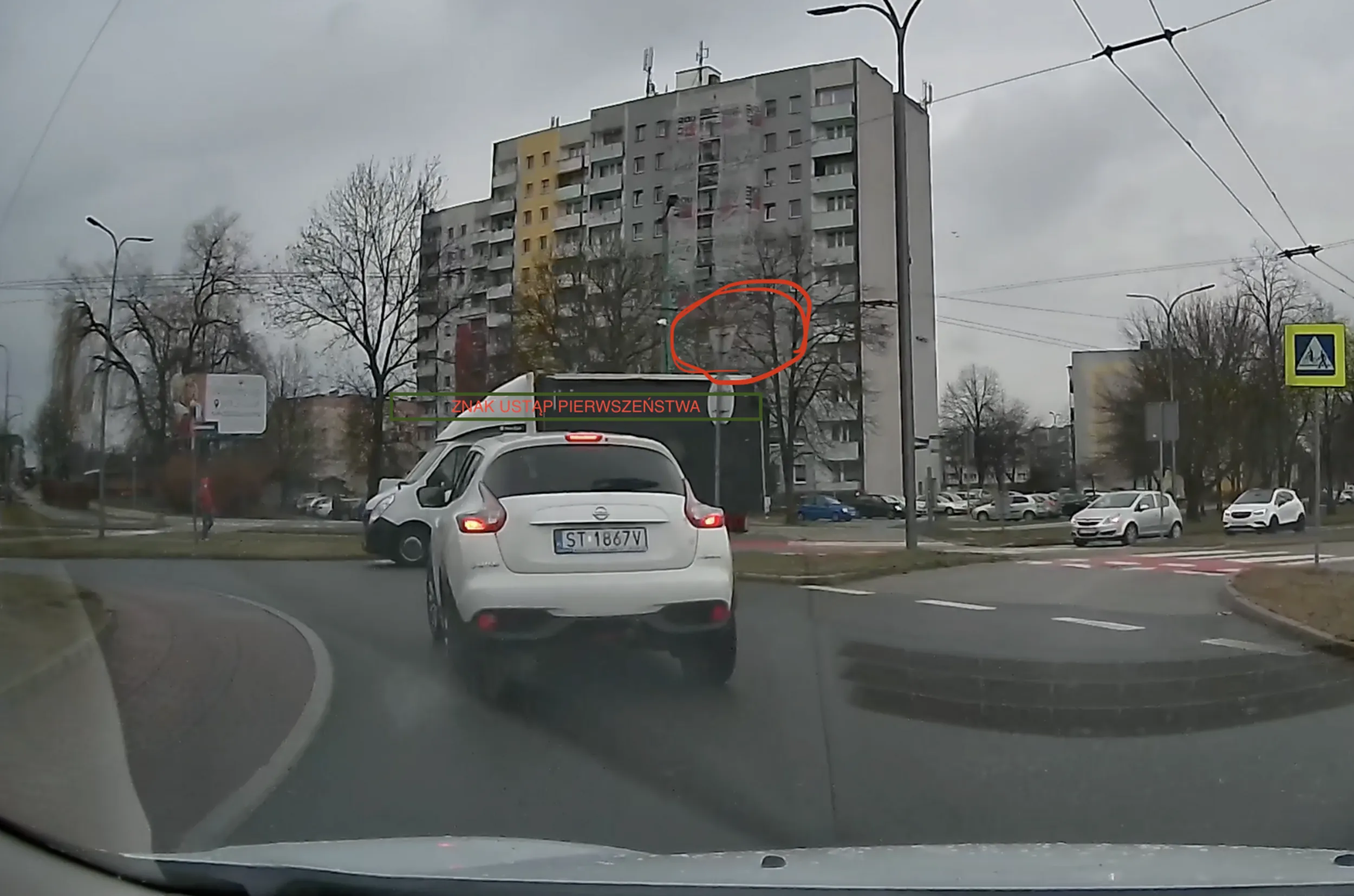 Ocena zachowania kierowcy na zdjęciu wskazuje na złe zachowanie, który może zagrażać bezpieczeństwu na rondzie. Kierowca białego samochodu marki Nissan bez uzasadnienia ustąpił pierwszeństwa na rondzie, pomimo że ciężarówka posiada znak przed wjazdem na rondo znak "Ustąp pierwszeństwa". Wyraźnie widać, że ciężarówka miała ustąpić pierwszeństwo pojazdą na rondzie, co oznacza, że kierowca Nissana naruszył przepisy drogowe. Takie działanie może być niebezpieczne i prowadzić do poważnych incydentów drogowych.