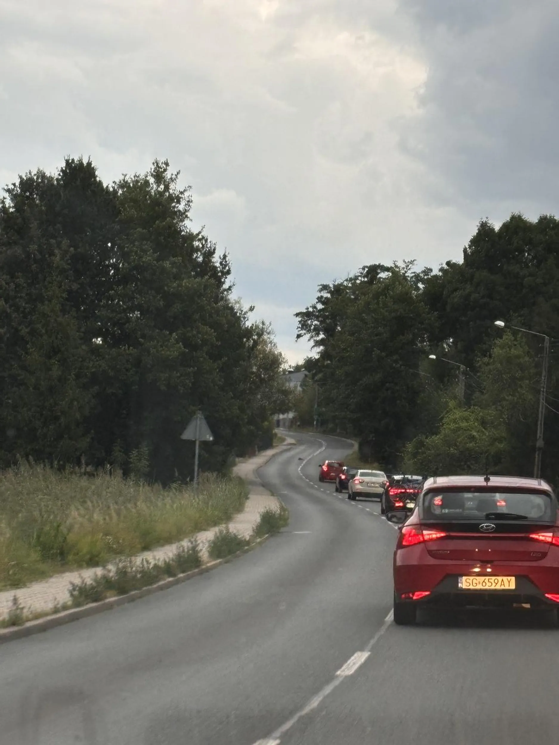 Walczy o życie za kółkiem, w miejscu, w którym ograniczenie prędkości i warunki na drodze umożliwiają płynną i dynamiczną jazdę skutecznie utrudnia innym uczestnikom ruchu drogowego życie, młoda dziewczyna w okularach za kółkiem (za nami na zdjęciu sznureczek ciągnął się dalej)