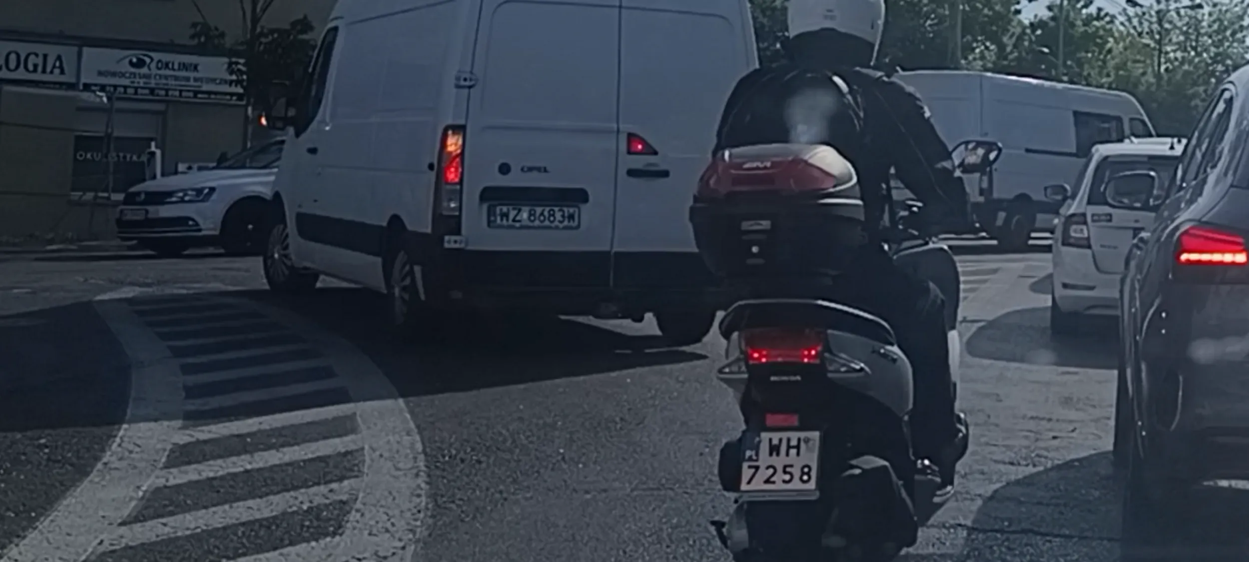 Bandyta na wraku skutera przepycha się w korku między autami, wyprzedza na podwójnej linii ciągłej przed przejściem dla pieszych i na samym przejsciu dla pieszych.