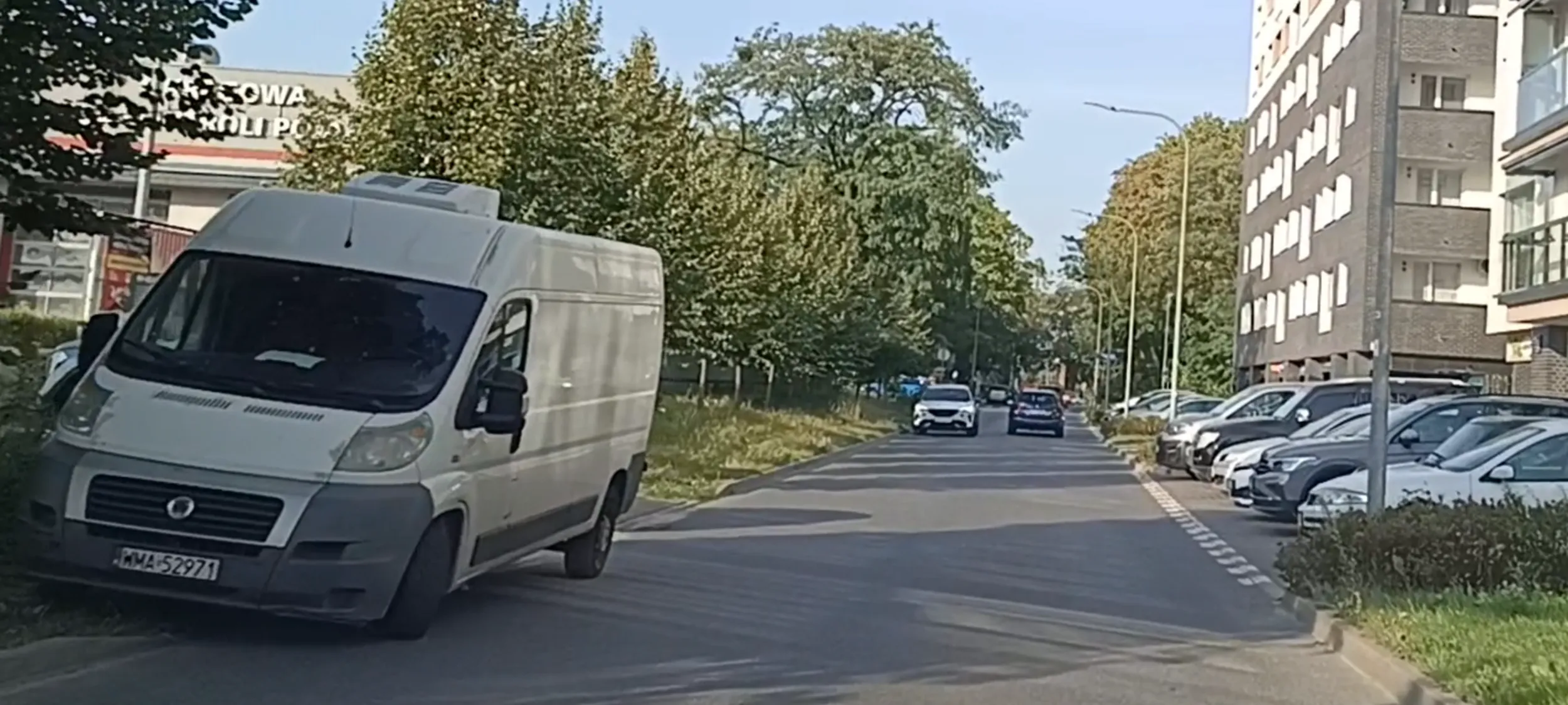 Wrak cały w rdzy porzucony na trawniku przy ulicy z zakazem zatrzymywania się i postoju