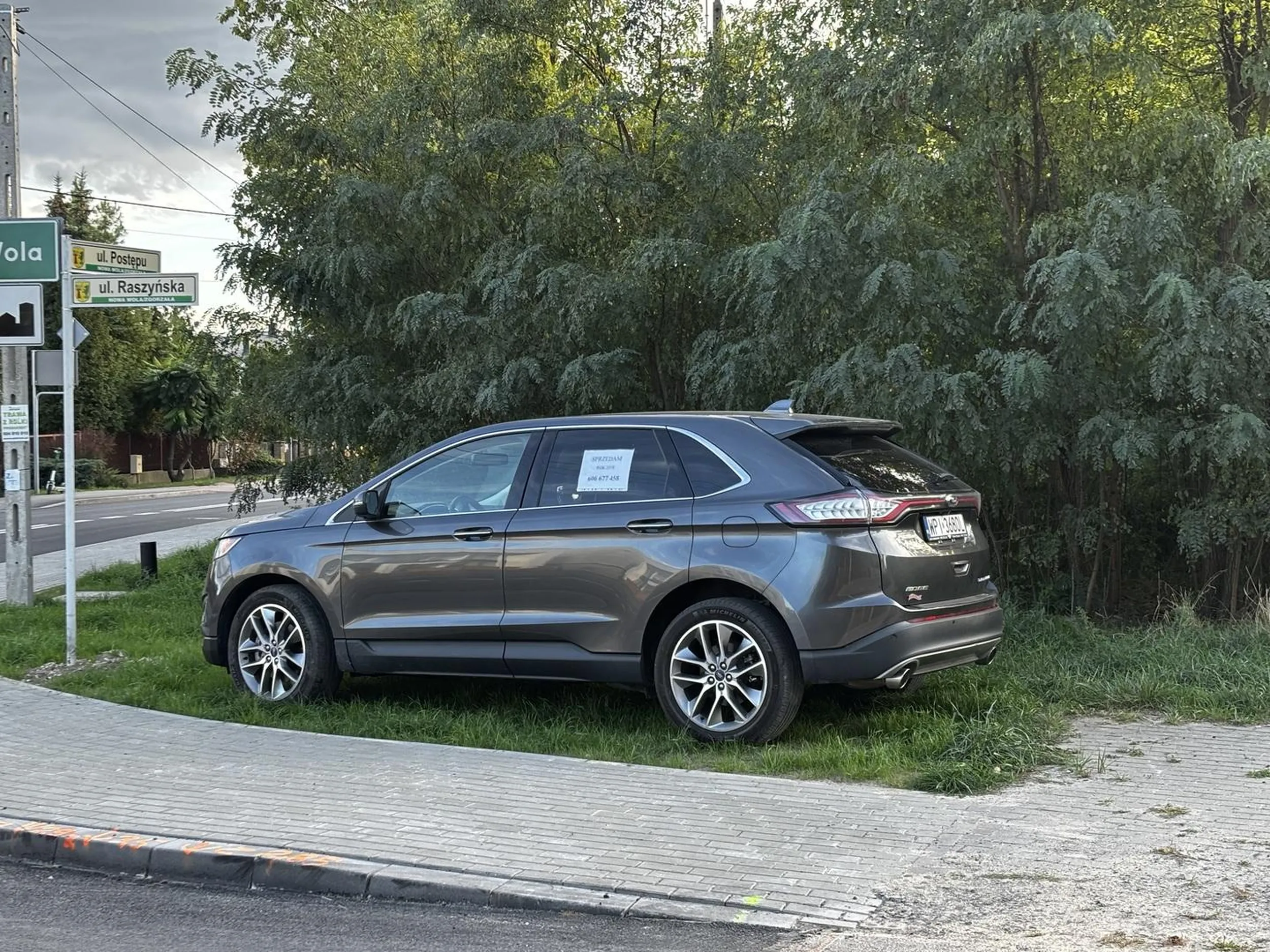 Wspaniały przykład niszczenia swojej okolicy.  Nowa trawa która urosła 2 tygodnie temu. Świeżo wyremontowana ulica. Trzeba postawić swoją bajadere na sprzedaż. Przejazd po pasach i chodniku, niszczenie zieleni, ograniczanie widoczności na skrzyżowaniu. Gratulacje ? jeszcze na? środku.