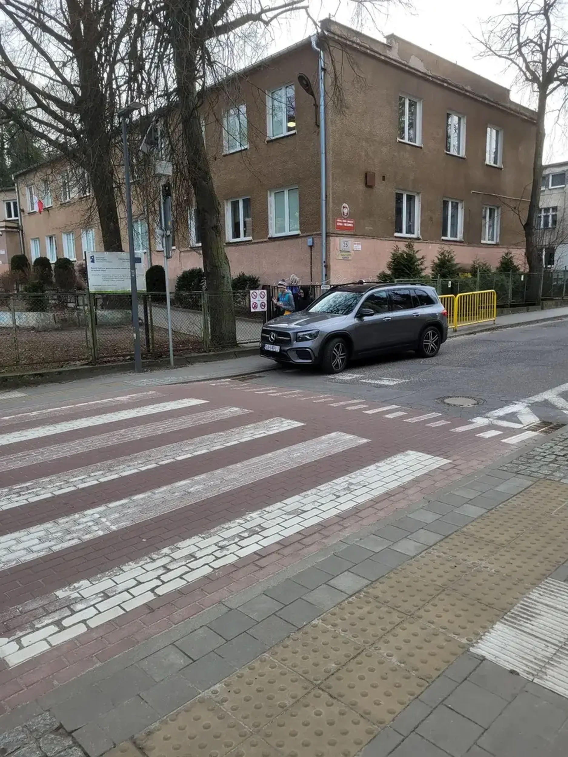 Parkowanie pod szkołą. Mamuśka czeka na bąbelka, a butów szkoda. Niebezpieczna sytuacją dla innych dzieci pieszych.