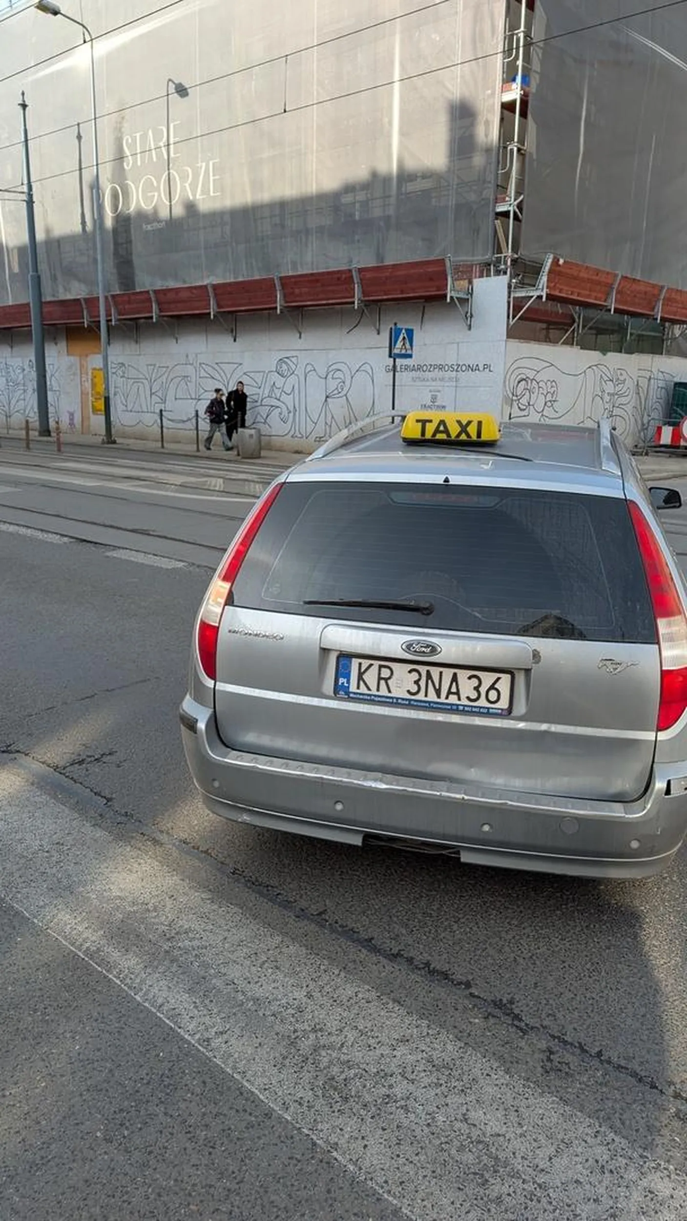 Taksówkarz, który zajeżdża drogę pieszym pomimo, że auto z drugiej strony stoi ustępując pierwszeństwa.