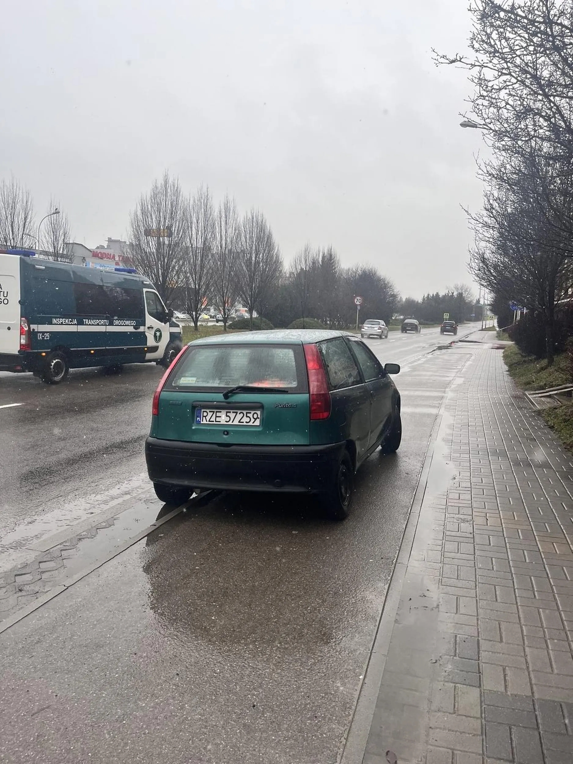 Na zdjęciu widać samochód zaparkowany na drodze rowerowej, co jest niezgodne z przepisami ruchu drogowego w Polsce. Droga rowerowa jest przeznaczona wyłącznie dla ruchu rowerzystów i nie wolno na niej zatrzymywać się ani parkować pojazdów, chyba że przepisy ruchu drogowego (lub oznakowanie) wyraźnie to dopuszczają, czego w tym przypadku nie widać. Art. 49 ust. 1 pkt 11 ustawy Prawo o ruchu drogowym stanowi, że zabronione jest zatrzymywanie pojazdu “na drogach dla rowerów”. Za takie parkowanie kierowca może otrzymać mandat karny, a w skrajnych przypadkach pojazd może zostać odholowany. Dodatkowo, parkowanie w ten sposób stwarza zagrożenie i utrudnia ruch rowerzystom, co może być szczególnie niebezpieczne w przypadku słabej widoczności, np. podczas opadów, jak na zdjęciu.