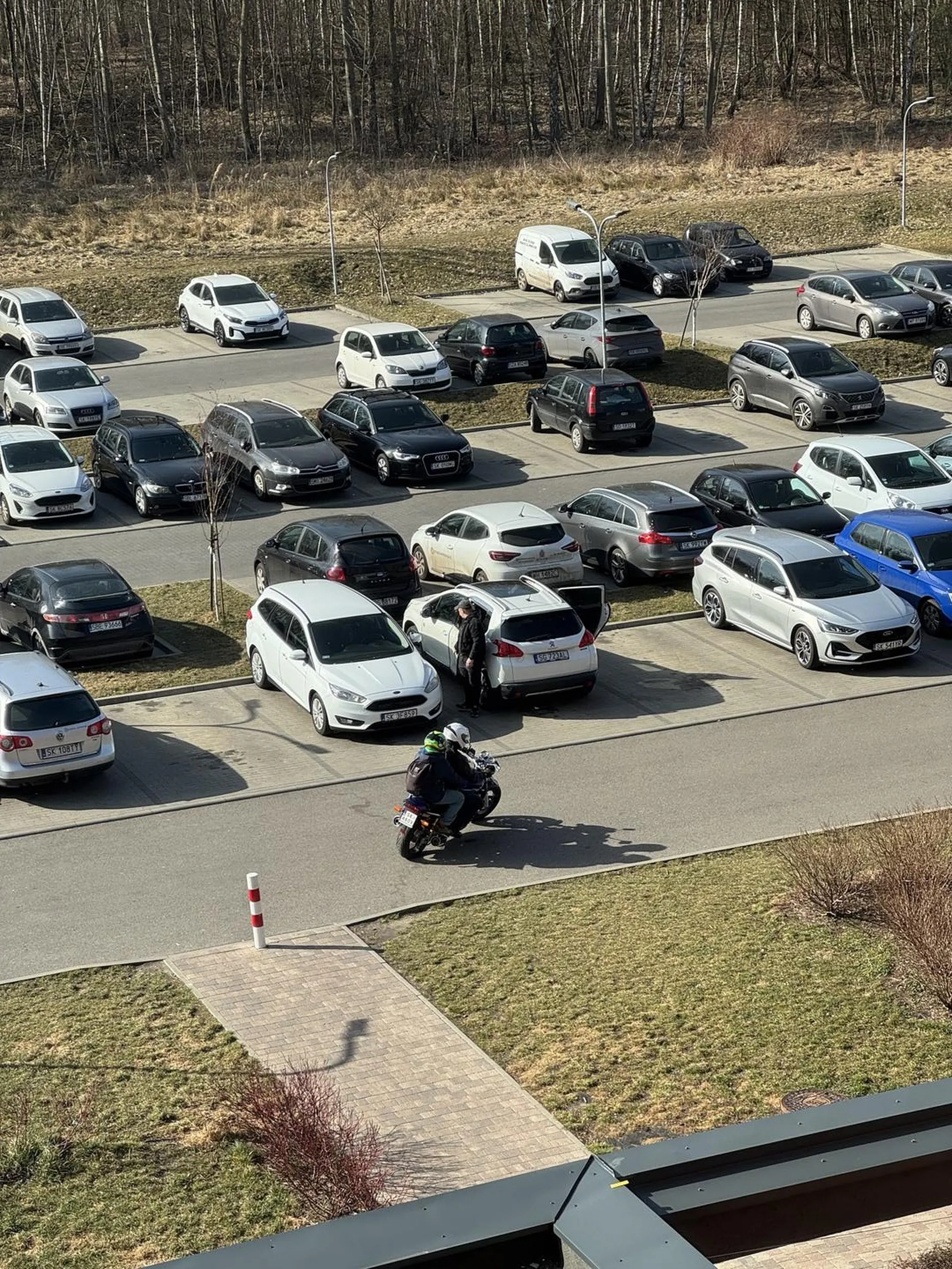 Motocyklista jeździ po chodnikach na wewnętrznym placu osiedla gdzie bawią się małe dzieci
