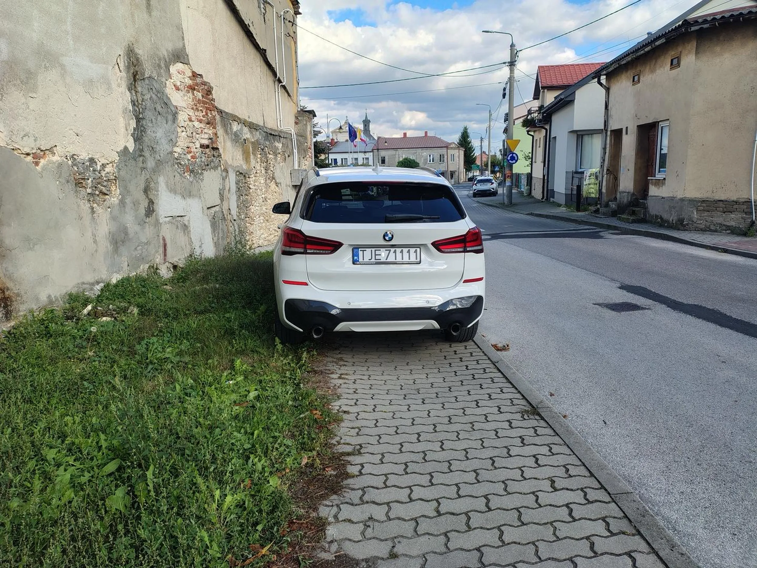Stoi na chodniku, nie da sie przejść, a ulice obok wielki parking