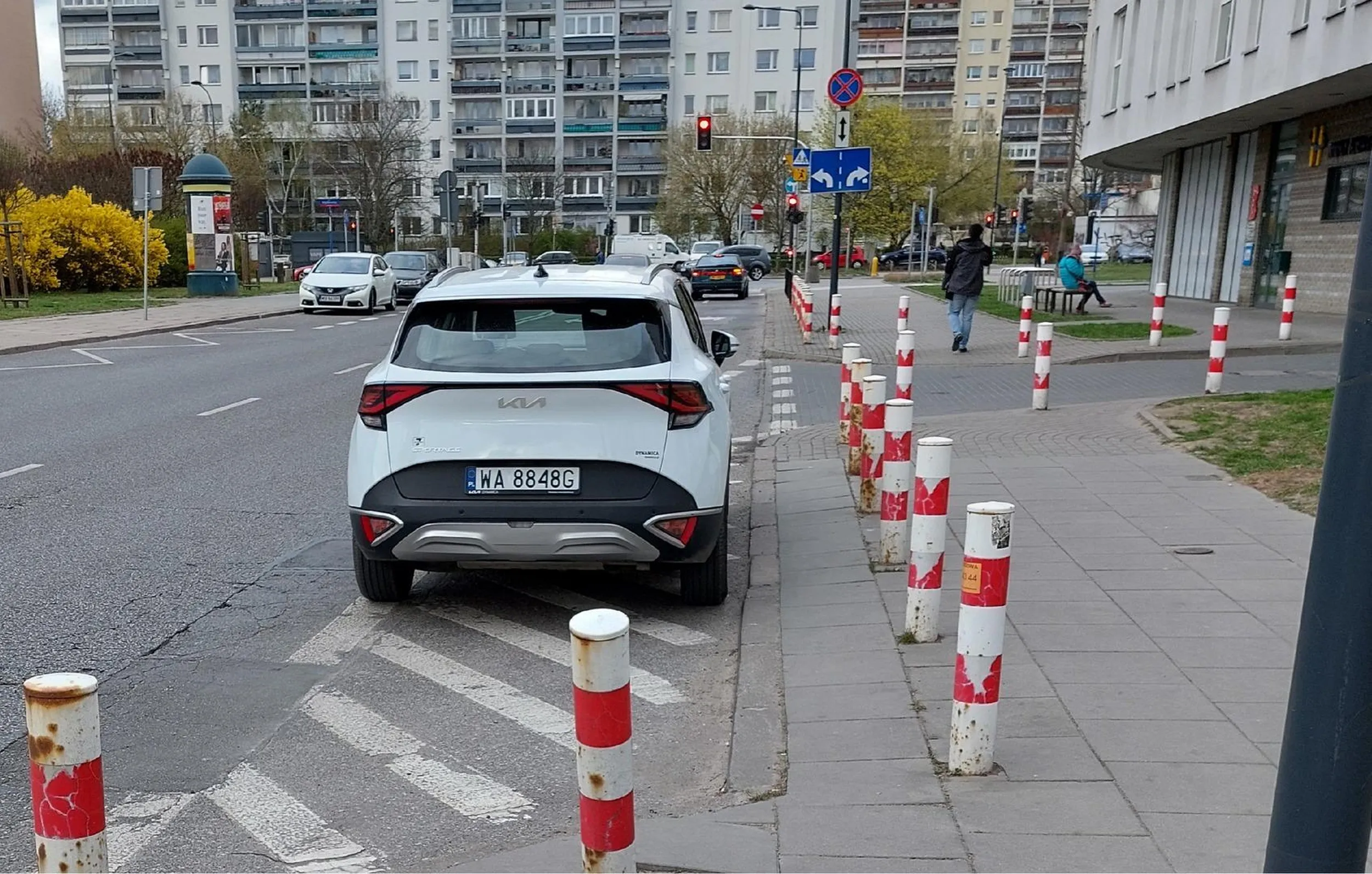 Paniusia nie wie, co oznaczają znaki namalowane na jezdni (znak P-21) i parkuje tam, gdzie jej wygodnie, mimo że jest to zabronione. Miejsce to: Warszawa, Białołęka, po lewej przystanek autobusowy Porajów 04, po prawej budynek przy ulicy Porajów, numery 12 i 14.