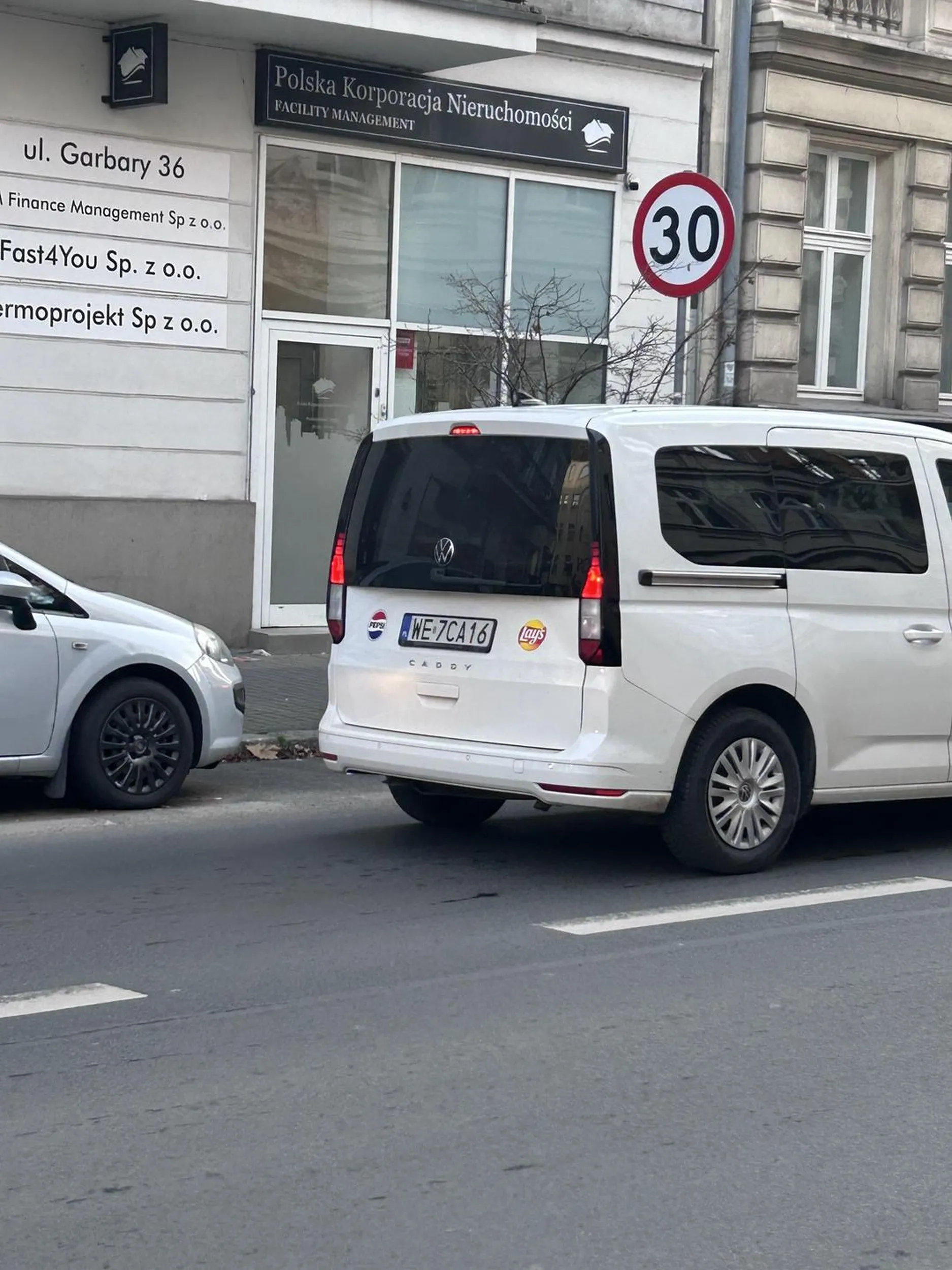Poznań Garbary. Młotek w okularach z tabletem przed kierownicą. Nie patrzy na drogę i czy ktoś przechodzi na pasach. Na vanie widać emblematy Pepsi i Lays czyli służbowe. Mandat już na firmę by nie był