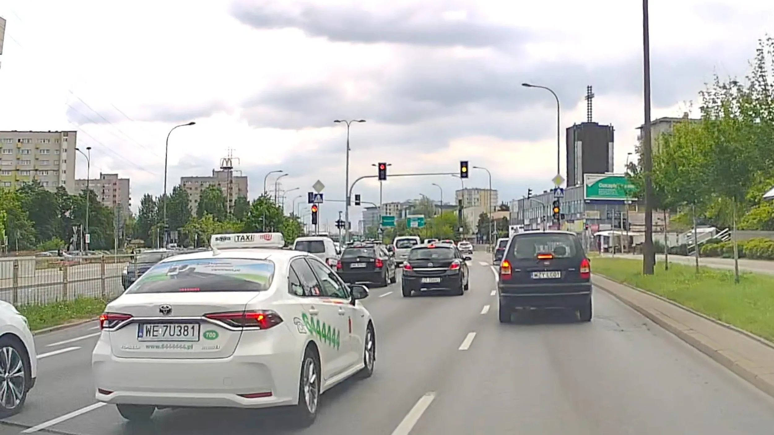 Taksówkarz SAWA Taxi widząc, że światło zmienia się na czerwone, zmienia pas na linii ciągłej i przejeżdża przez skrzyżowanie na czerwonym.