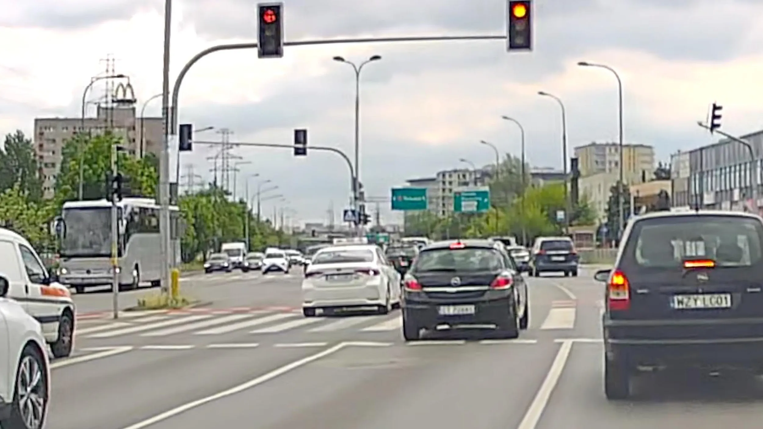 Taksówkarz SAWA Taxi widząc, że światło zmienia się na czerwone, zmienia pas na linii ciągłej i przejeżdża przez skrzyżowanie na czerwonym.