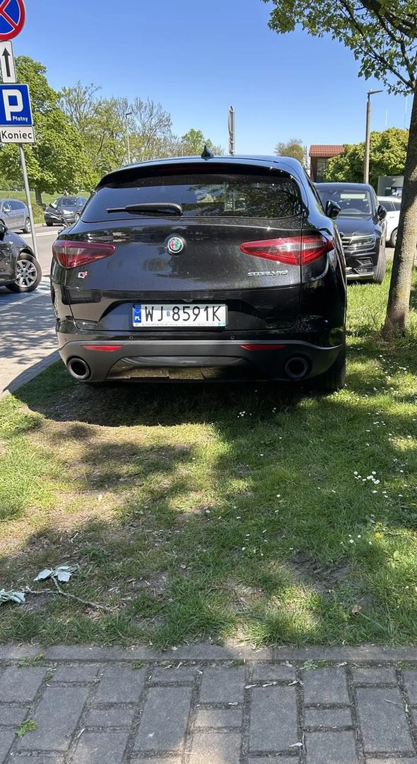 Kierowca pojazdu marki Alfa Romeo (rejestracja WJ 8591K) przejechał przez chodnik i zaparkował na trawniku, bezpośrednio na korzeniach drzewa. Takie parkowanie łamie przepisy, niszczy zieleń i świadczy o braku szacunku dla przestrzeni publicznej oraz pieszych. Zdecydowanie zasługuje na negatywną ocenę.
